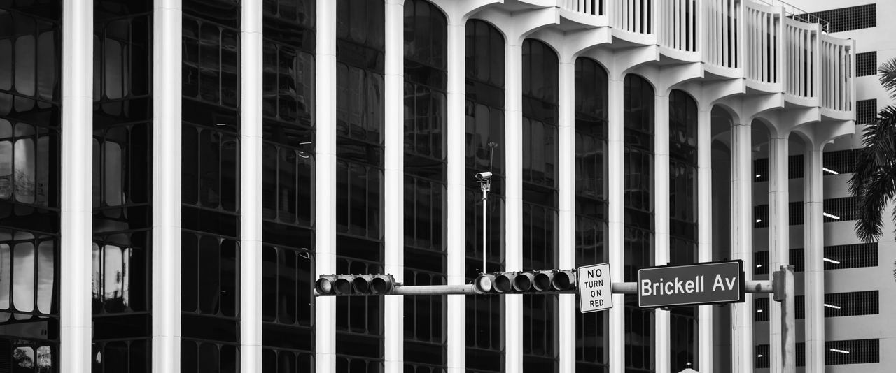 White columns of an office building on Brickell Avenue, behind a traffic signal and a Brickell Av street sign